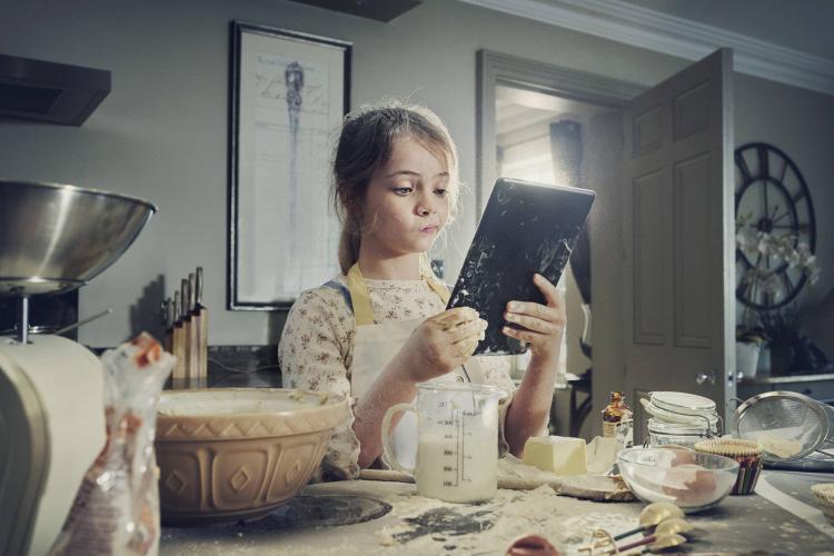 Ung jente baker p&aring; kj&oslash;kkenet og holder en Talkmore-enhet